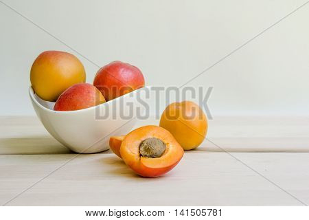 Apricots in white bowl with one apricot cut open.