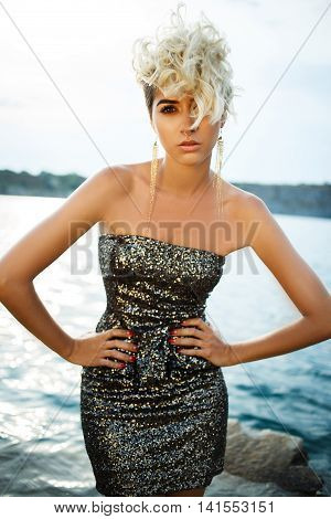 High fashion look.glamor beautiful sexy stylish blond Caucasian young woman model with bright makeup with perfect sunbathed clean skin in darkgold dress posing on beach