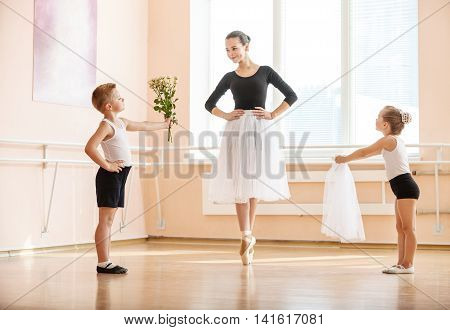 At ballet dancing class: young boy and girl giving flowers and veil to older student while she is dancing en pointe
