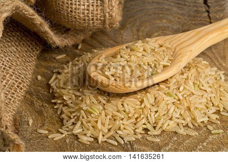 Natural brown uncooked rice in wooden spoon on wood table