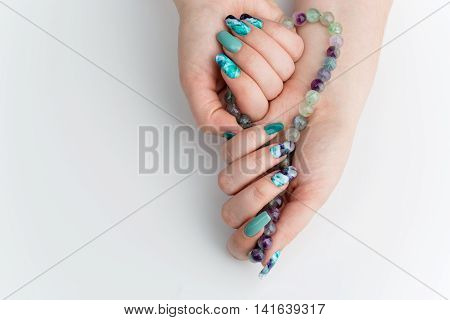 Closeup of woman nails with creative purple and green manicure. Fluorinit print. Natural stone beads. Copy space.