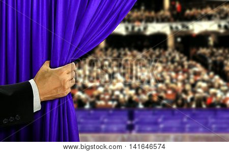 Hand opening blue stage curtain and audiance