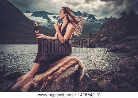 Nordic goddess in ritual garment with hawk near wild mountain lake in Innerdalen valley, Norway.