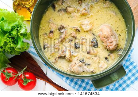 Fricassee of chicken with mushrooms in ceramic pot on white wooden table. Top view