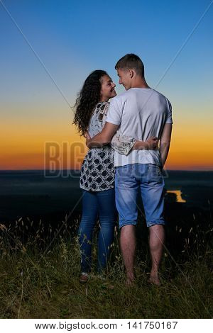 romantic couple embrace at sunset, beautiful landscape and bright yellow sky, love tenderness concept, young adult people backside