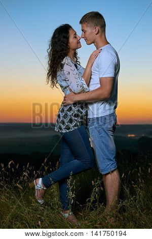 romantic couple embrace at sunset, beautiful landscape and bright yellow sky, love tenderness concept, young adult people
