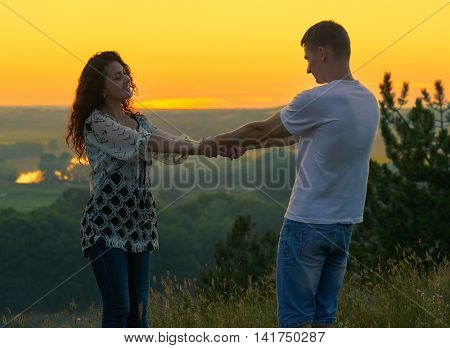 romantic couple holding hands at sunset on outdoor, beautiful landscape and bright yellow sky, love tenderness concept, young adult people