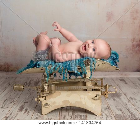 cute little baby with legs up lying on child scales on wooden floor