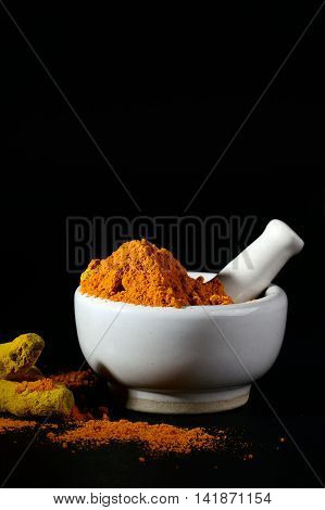 Turmeric powder in mortar with pestle and roots or barks on black background