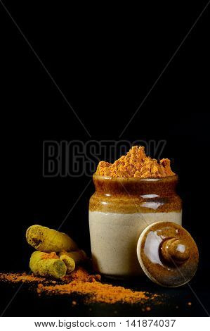 Turmeric powder in clay pot with roots or barks on black background