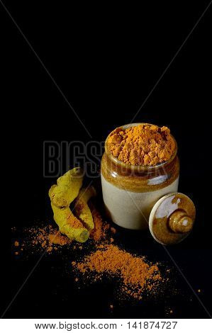 Turmeric powder in clay pot with roots or barks on black background