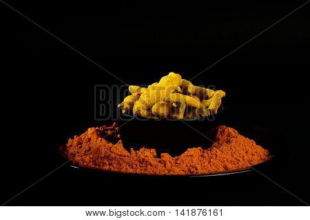 Turmeric powder and roots or barks on black background
