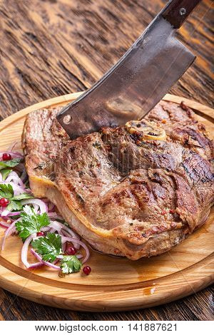 Medium rare grilled Beef steak Ribeye with onion on cutting board on dark wooden background. carving knife is in steak.
