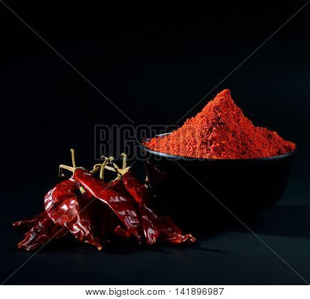 chilly powder in black bowl with red chilly, dried chillies on black background