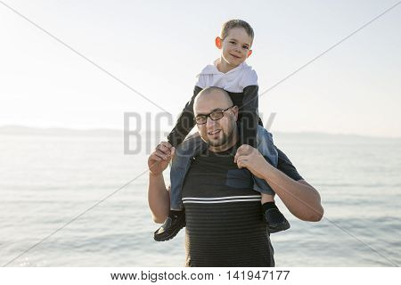 A Son on father shoulders at the beach having fun at sunset together