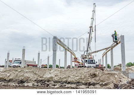 Mobile crane is operating and worker is assembly concrete joist in high place. Height worker is placing truss on building skeleton.
