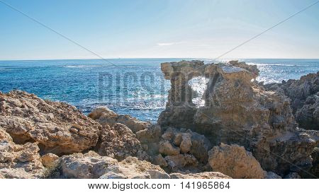 Natural limestone window and rugged coastal rock formation with the Indian Ocean seascape under a blue sky at Point Peron in Rockingham, Western Australia