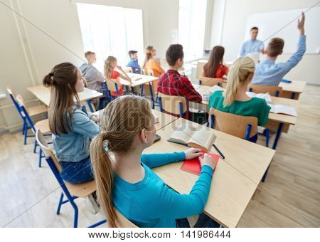 education, high school, teaching, learning and people concept - group of happy students raising hands and teacher in classroom
