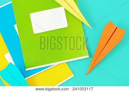 Set Of Colorful Exercise Books With Paper Airplane Blue Background. Top View Minimalist Education Ba