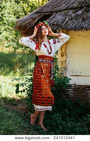 Beautiful Ukrainian Girl In National Clothes Embroidered On A Wooden Hut In The Summer
