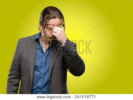 Handsome young man with sleepy expression, being overworked and tired, rubbes nose because of weariness