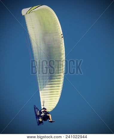 Hang Glider Flies High In The Blue Sky With A Person Sitting As A Pilot And  With Old Vintage Effect