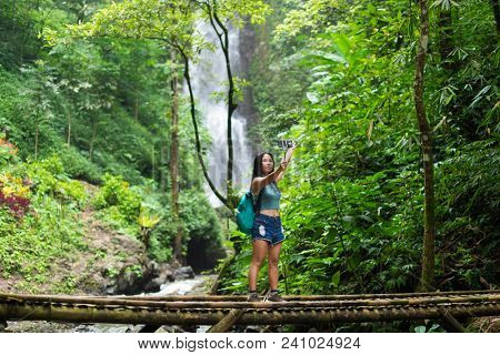 Tourist woman taking a selfie on a bamboo bridge near the Red Coral waterfall in the Munduk jungle, Bali, Indonesia