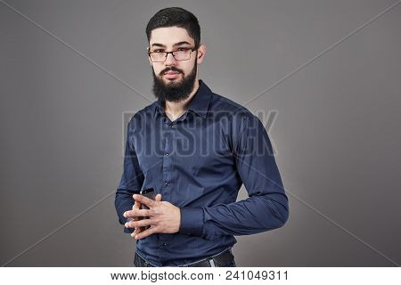 Happy Man In Glasses With Smartphone On Hands On Gray Background.