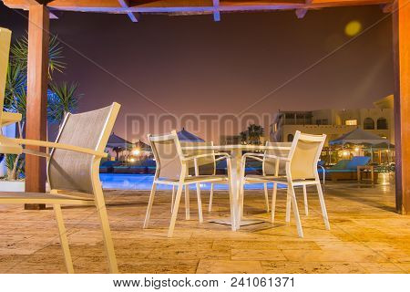 Territory Of Hotel In South Country In A Night. Table And Chairs Near Sweeming Pool By Light