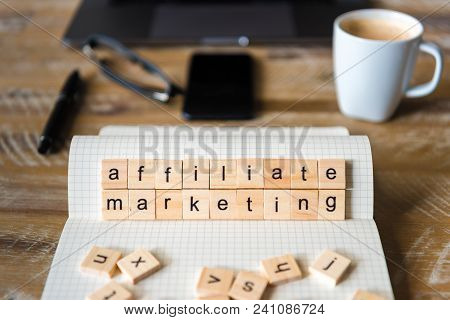 Closeup On Notebook Over Table Background, Focus On Wooden Blocks With Letters Making Affiliate Mark