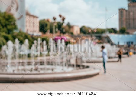 Blurred Background With Peolple Walking Around Fountains At The City Centre.