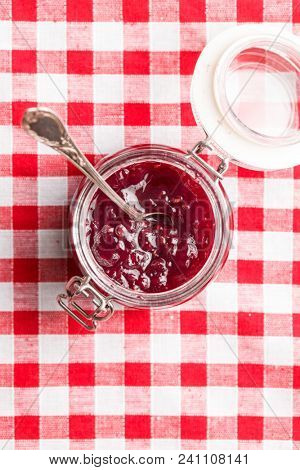 Raspberry jam jelly in jar on checkered tablecloth.