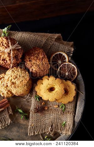 Conceptual Composition With Assortment Of Cookies, Cinnamon Sticks Bunch And Dried Oranges With Burl