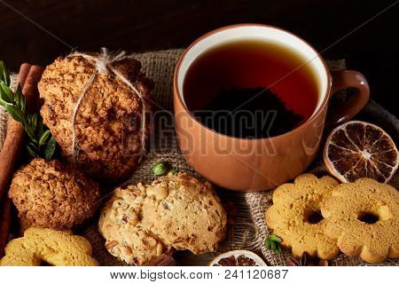 Festive Composition With A Mug Of Hot Tea, Assortment Of Cookies, Cinnamon Sticks Bunch And Dried Or