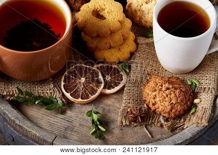 Conceptual Festive Composition With Two Cups Of Hot Tea, A Large Set Of Cookies, Cinnamon Sticks Bun