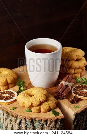 Christmas Concept With A White Porcelain Cup Of Hot Tea, A Large Set Of Cookies, Cinnamon Sticks Bun