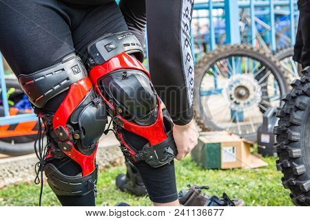 Man Puts Protection On His Knees For Motorsport, Black Red, Close-up