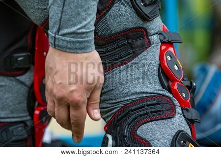 Man Puts Protection On His Knees For Motorsport, Black Red, Close-up
