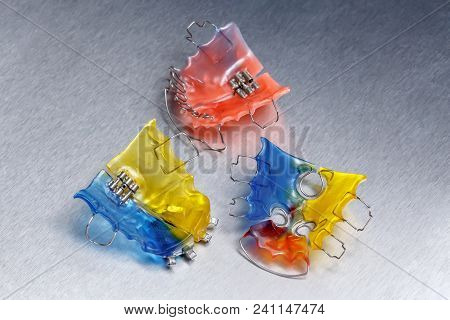 Three Colorful Dental Braces Or Retainers For Teeth On Metall Background, Closeup