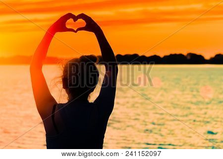 The Silhouette Of The Girl Against The Evening Sun, Red Sunset Makes The Heart Hands To The Sun