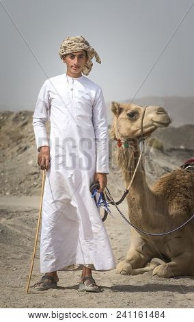 Ibri, Oman, 28th April 2018: Young Bedouin Man With His Camel In A Countryside Of Oman