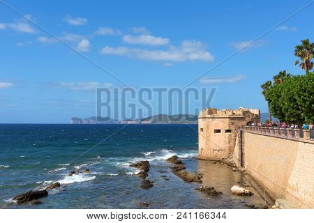 ALGHERO, ITALY -SEPTEMBER 19, 2017: People at the surrounding wall, next to the sea, of the Centro Storico, the old town of Alghero, in Sardinia, Italy, highlighting the San Giacomo tower