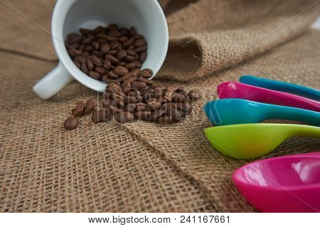 Loose Roasted Coffee Beans, White Porcelain Coffee Mug And Color Plastic Dose Measuring Spoons On Ju
