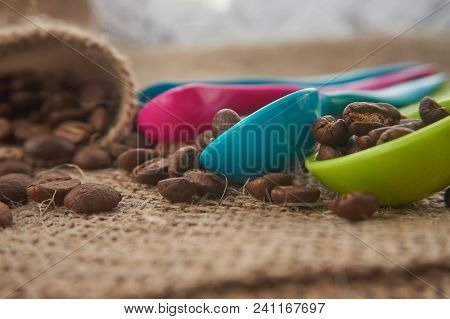 Loose Roasted Coffee Beans And Color Plastic Dose Measuring Spoons On Jute Sack. Conceptual Of Recom