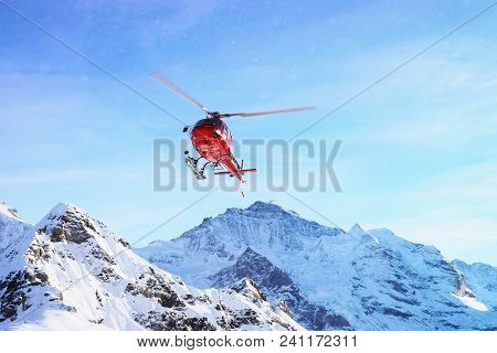 Maennlichen, Switzerland - December 31, 2013: Red Helicopter Flying Near Swiss Alps Mountain Maennli
