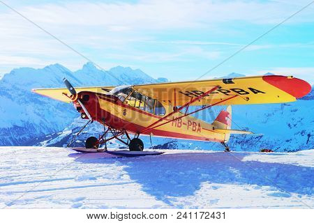 Maennlichen, Switzerland - December 31, 2013: Yellow Airplane In Mountain Alps Peaks, Maennlichen In