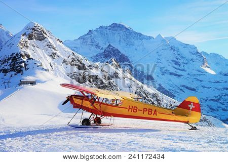 Maennlichen, Switzerland - December 31, 2013: Yellow Airplane On Mountain Alpine Peaks In Maennliche
