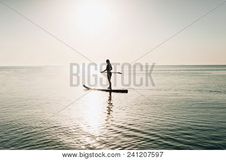 Silhouette Of A Sexy Athletic Girl Who Swims On Kayaks To Meet The Sun And Holds An Oar In Hands