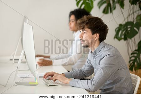Young Employee Focused On Computer In Multiracial Shared Office, Serious Guy Programmer Or Web Desig