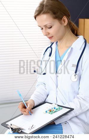 Woman Doctor Write Prescription While Sitting In Hospital Office. A Lot Of Various Colored Pills Liy